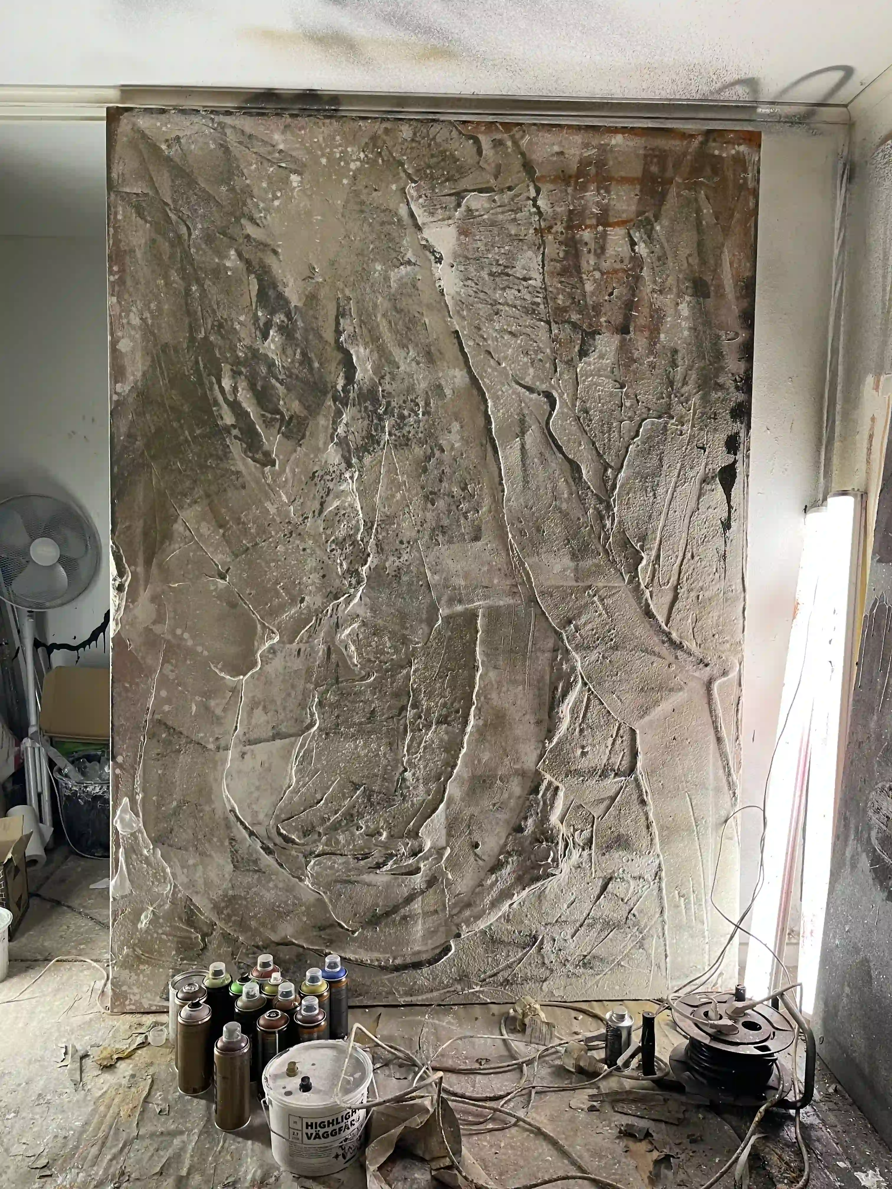 Canvas painting leaning against a studio wall, with materials scattered around